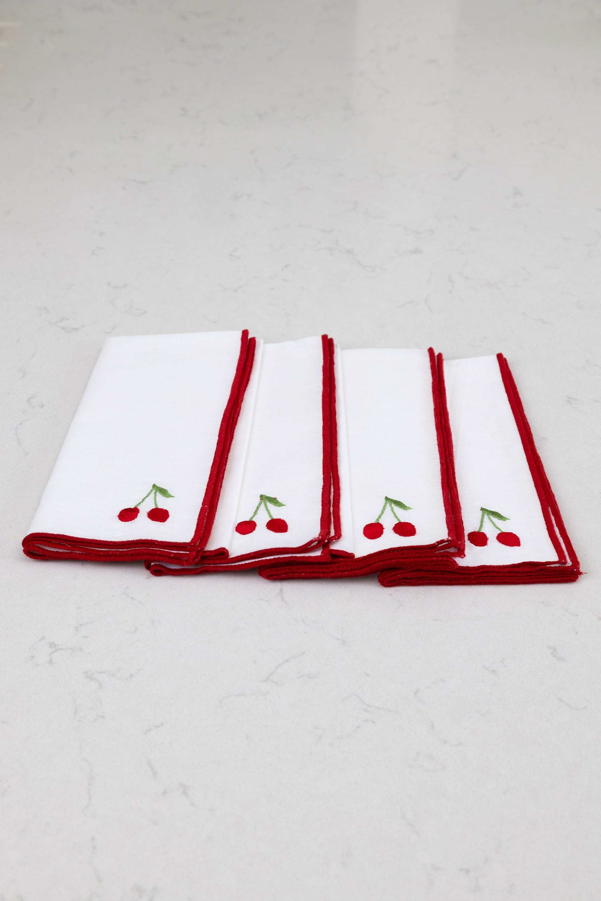 Set of four white napkins with red borders and cherry designs on a white background