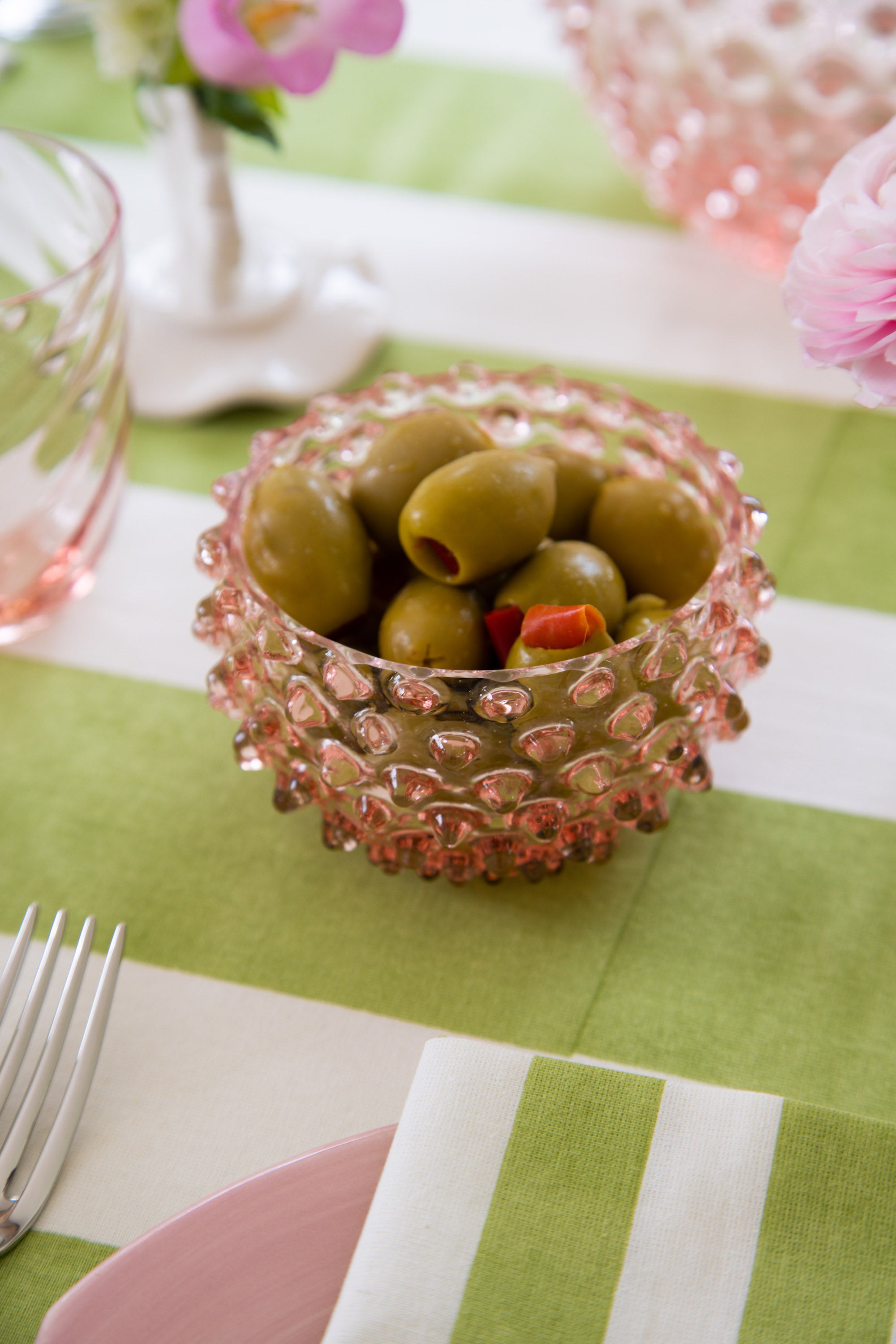 Small pink hobnail bowl on a green and white striped table cloth