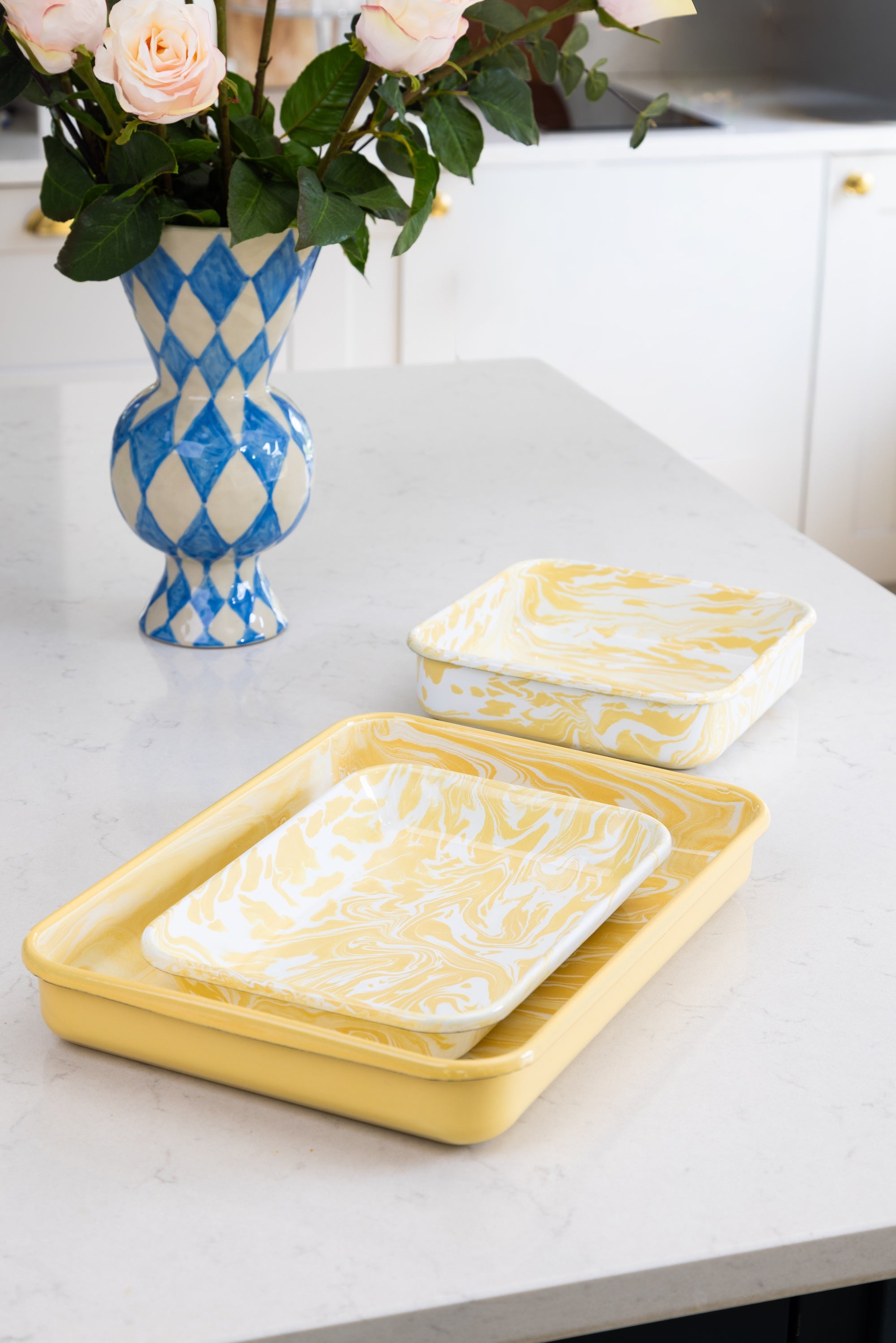 Yellow ceramic trays with white marbled design on a kitchen counter with a decorative vase of flowers.
